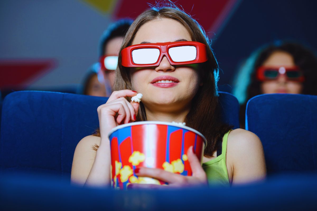 persona che guarda film al cinema con pop corn e occhiali